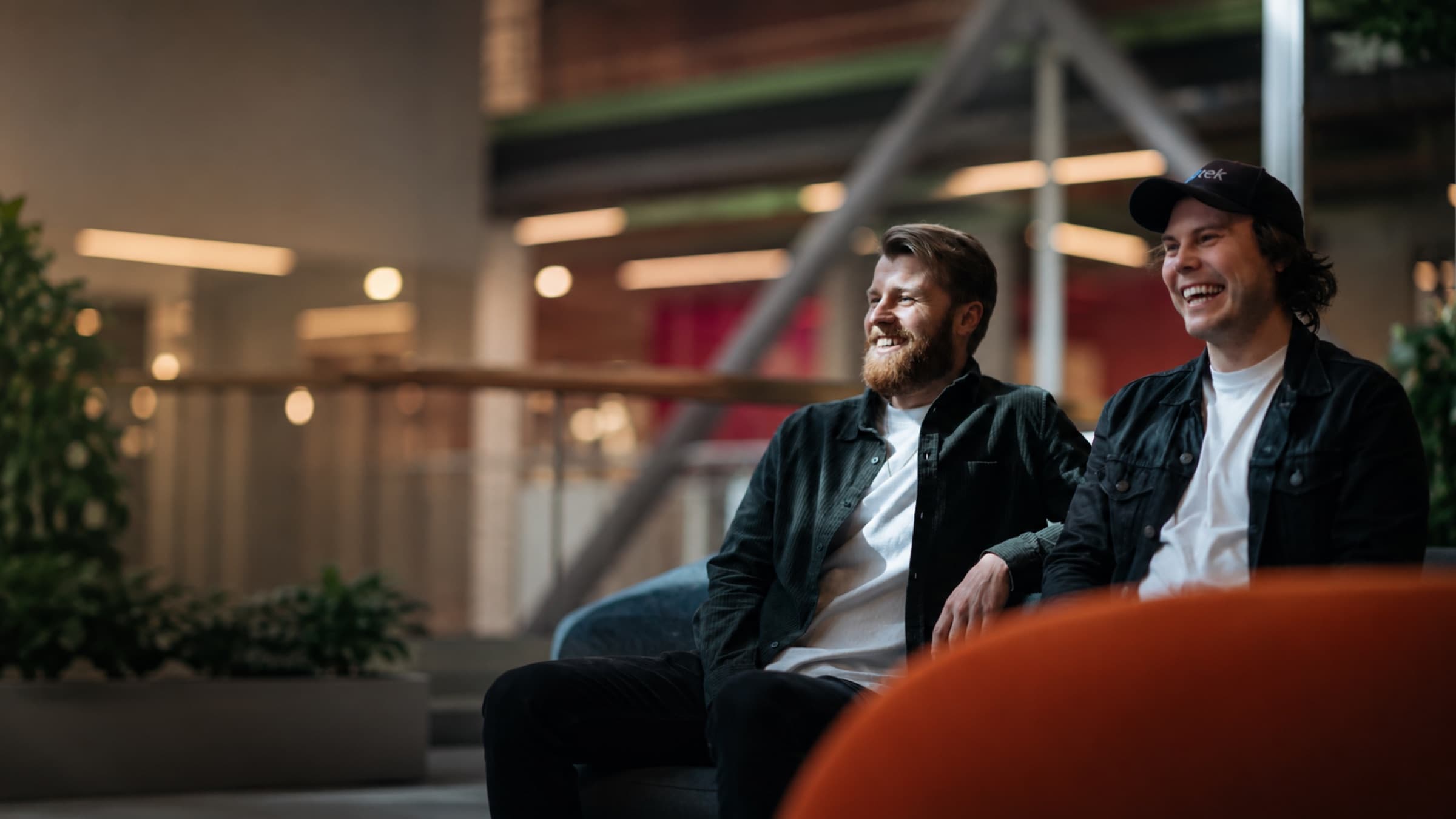 Altek founders Jon-Fredrik Hopland and Kristoffer S. Pedersen sitting together on a couch, laughing, in a warmly lit hotel lobby.