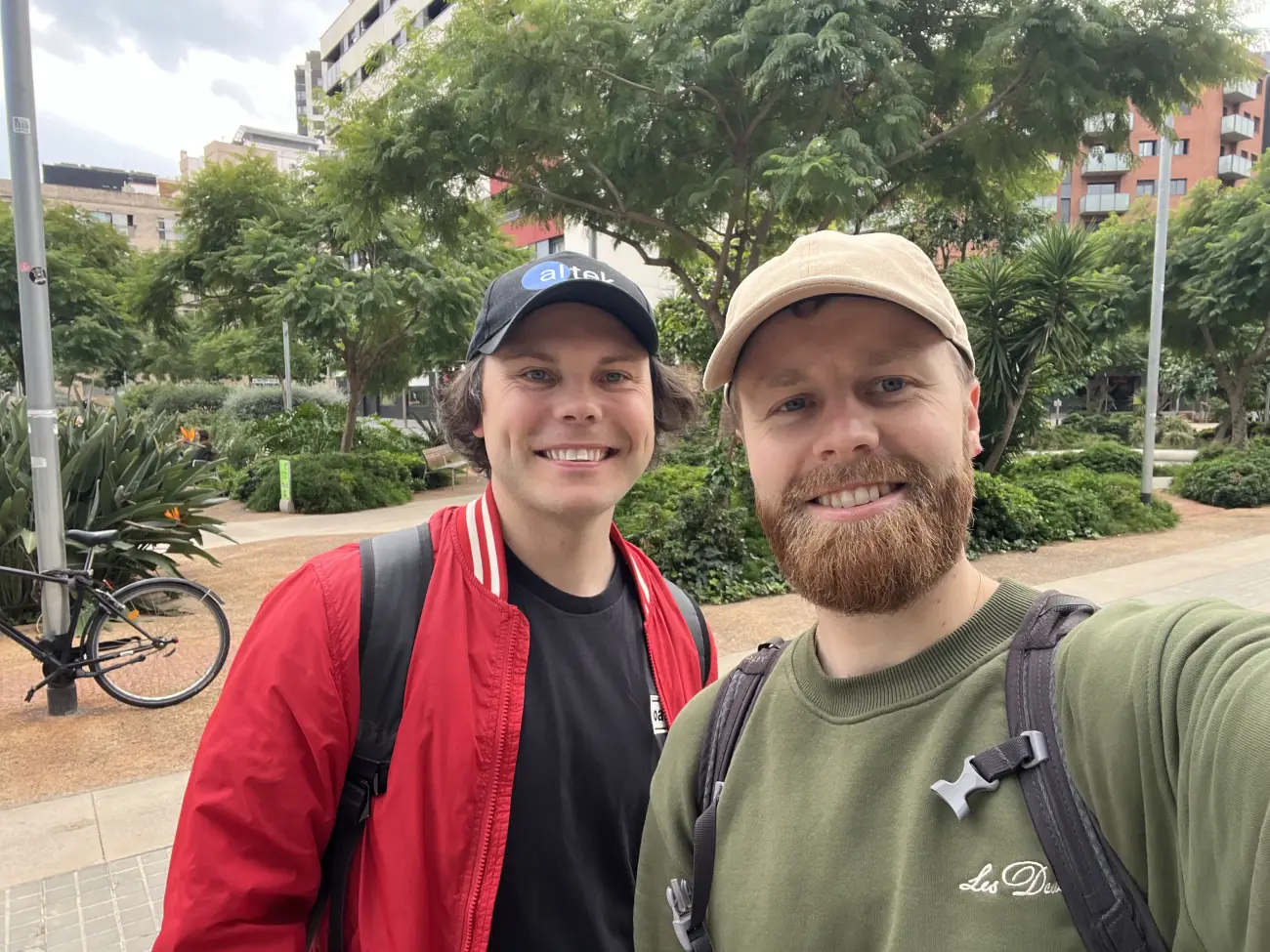 The two founders taking a selfie together in a leafy city park, both wearing backpacks.