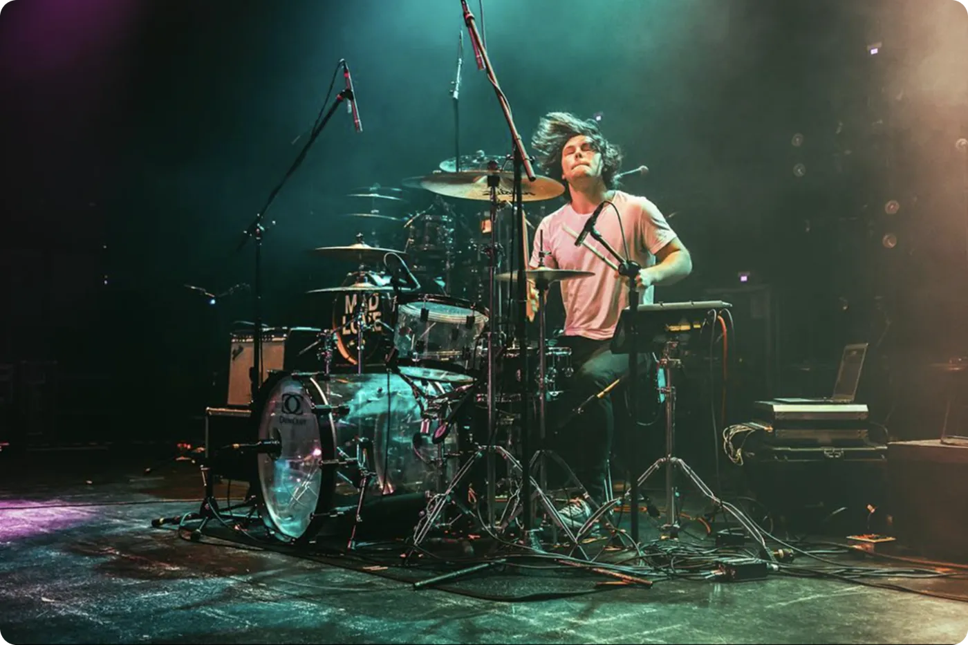Jon-Fredrik playing drums on a concert stage under teal and purple lights.