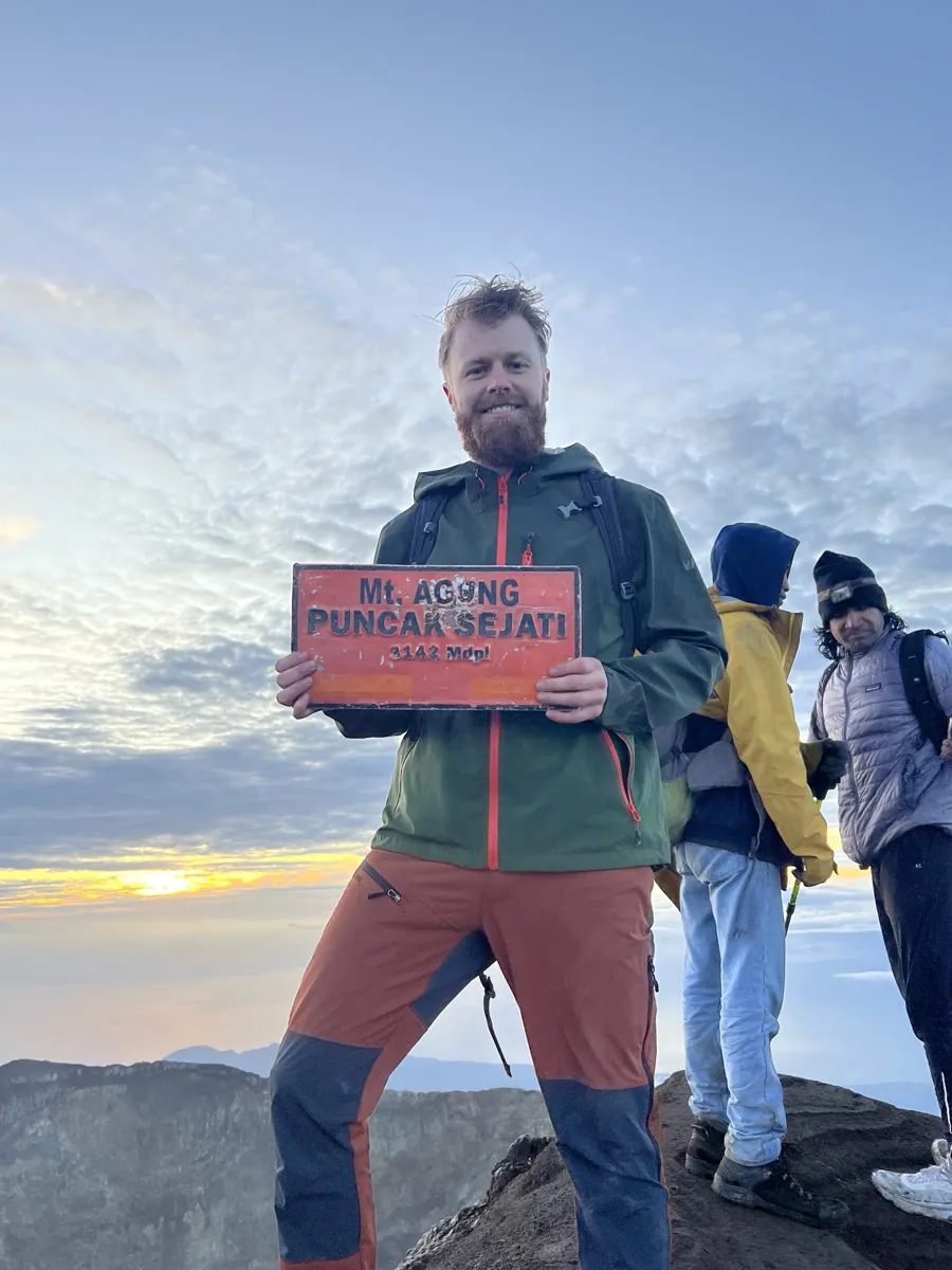 Kristoffer at the summit of Mount Agung at sunrise, holding the summit sign.