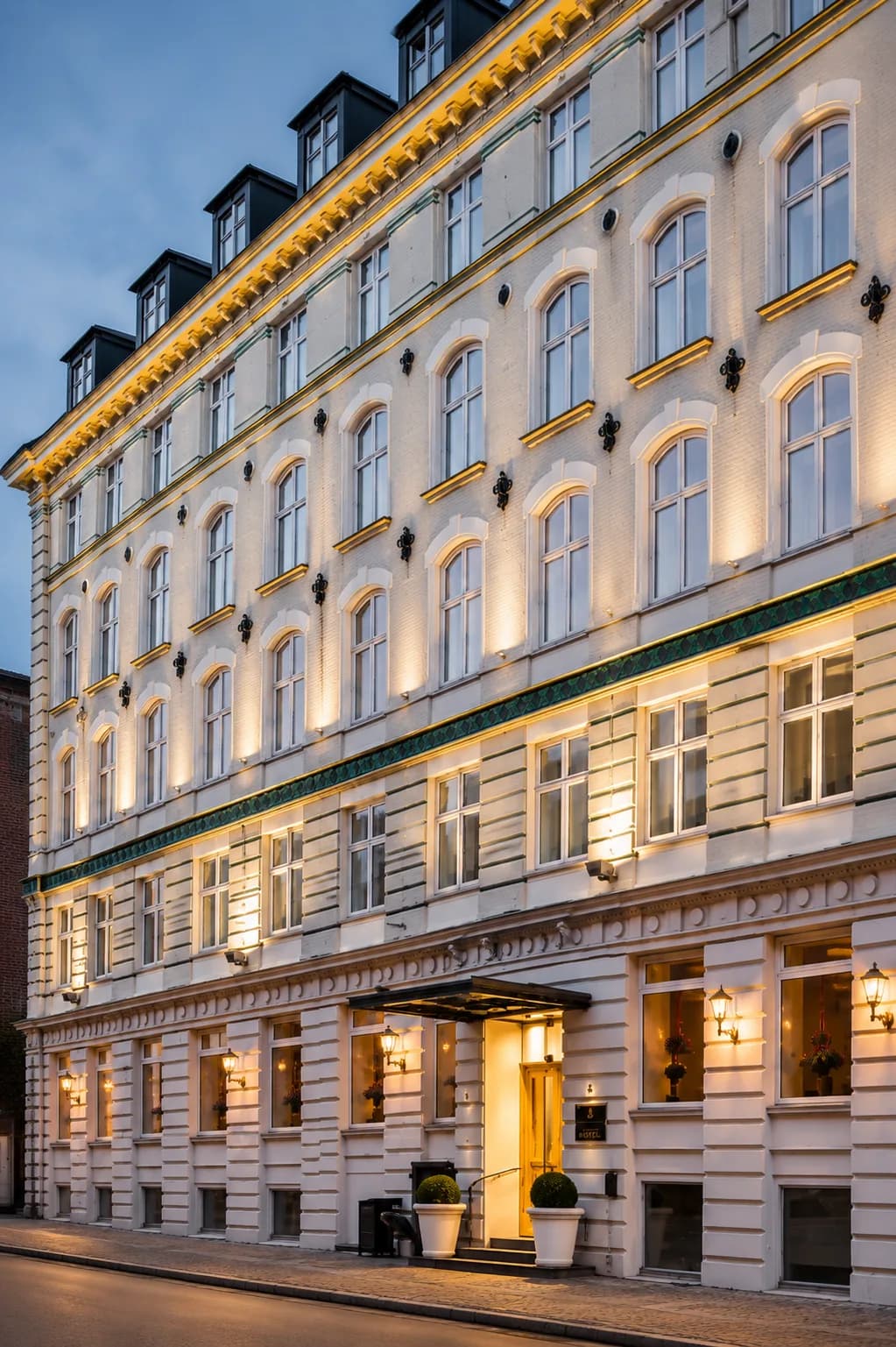 The lit facade of a classical city hotel at dusk.