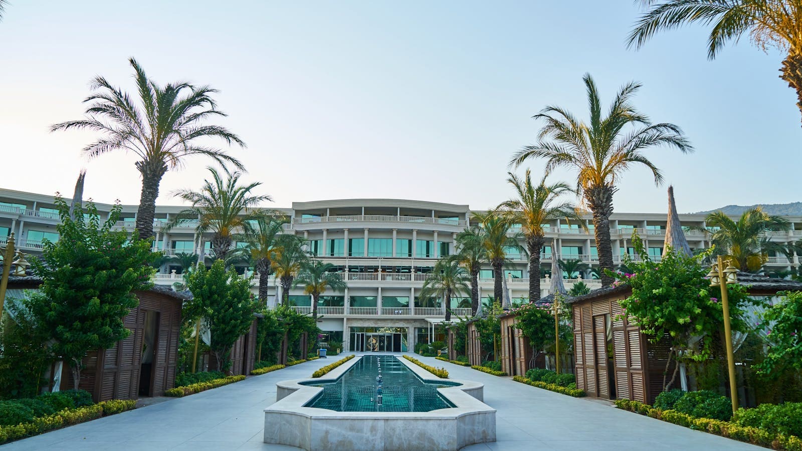 Stunning luxury resort with a long swimming pool flanked by palm trees and a modern hotel façade — one of many properties a hotel group standardizes with shared AI.