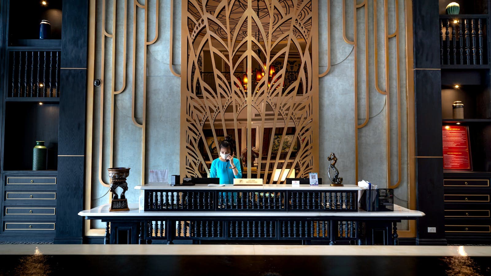 Luxurious hotel reception with intricate decorative panel and a receptionist at work — the front-office workflow Altek's email automation slots into.