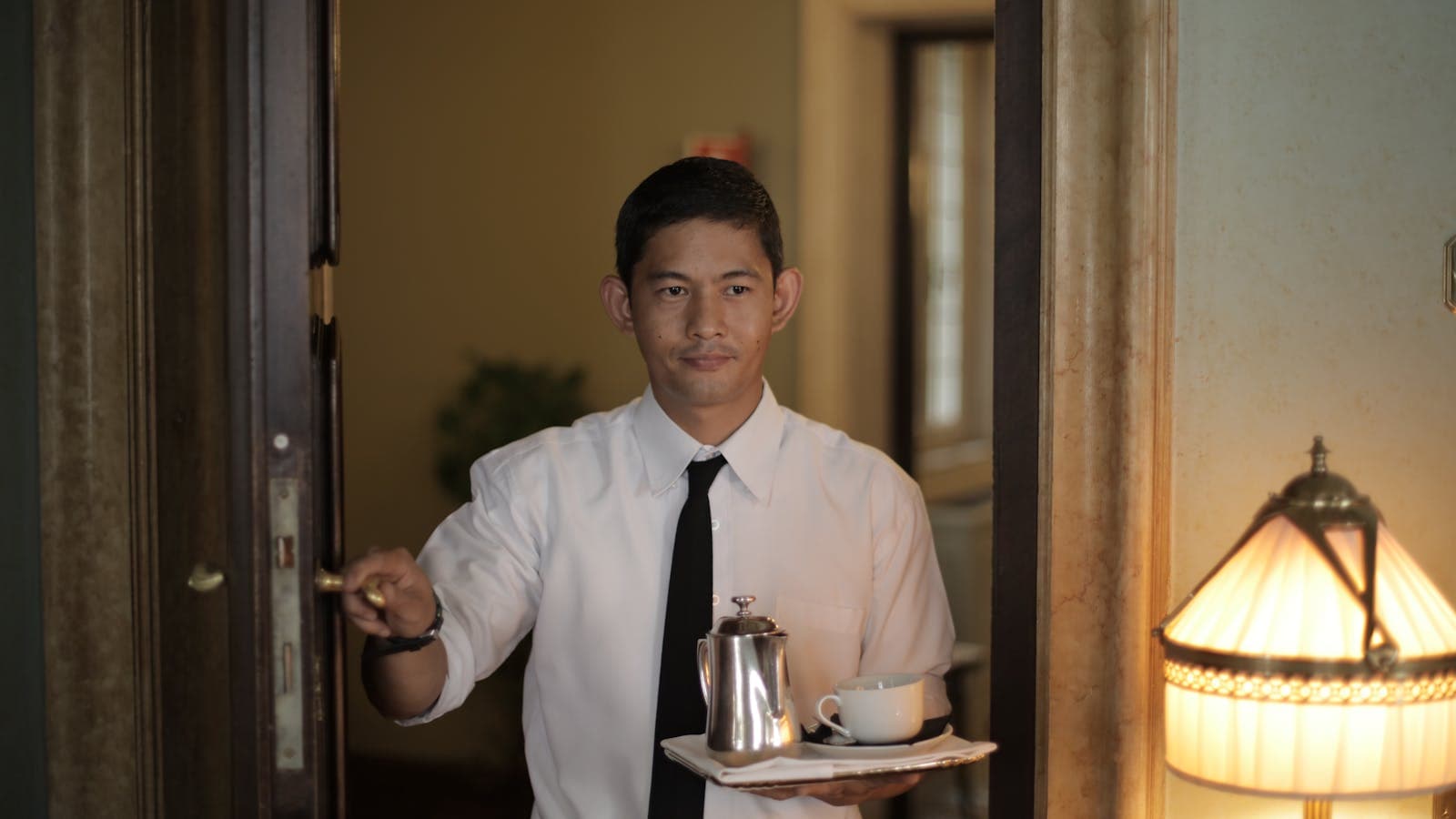 Hotel staff member opening a guest-room door carrying a coffee tray — the personal guest service an AI concierge supports rather than replaces.
